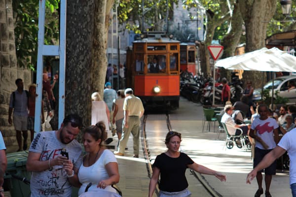 Sóller tram crossing the town among people sitting on a terrace
